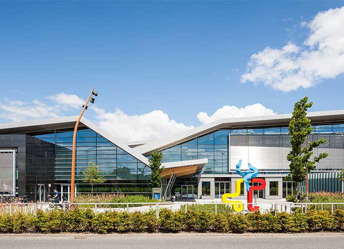 A large glass building with a colourful sculpture outside.